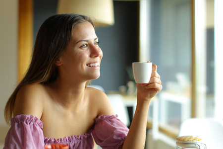 Happy teen holding coffee cup looking through a window at home and smilingの写真素材