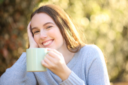 Happy woman looks at camera holding coffee cup in a parkの写真素材