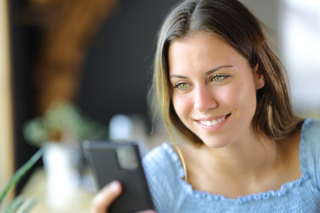 Happy teen checking cell phone in a house or restaurantの写真素材