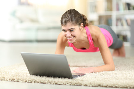 Teen doing online guided exercises using laptop on the floor at homeの写真素材