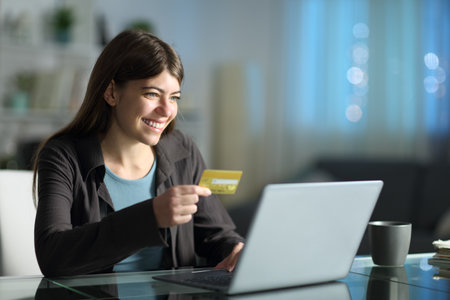 Woman buying online using credit card and laptop at home in the nightの写真素材