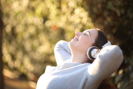 Profile of a happy woman relaxing listening audio with headphone on a bench in a parkの写真素材