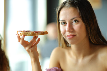 Woman looks at camera holding bread with jam in a restaurantの写真素材