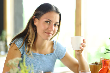 Satisfied woman holding coffee mug in a restaurant posing looking at cameraの写真素材