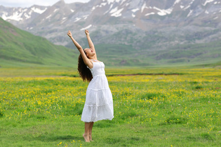 Excited woman in white dress raising arms in natureの写真素材