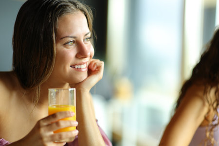Happy woman holding orange juice glass at breakfast in a restaurantの写真素材