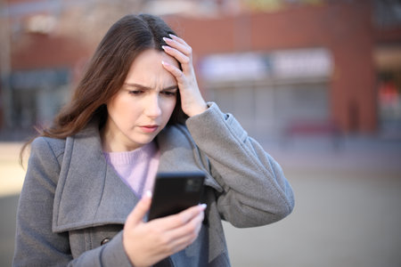 Worried woman checking smart phone content in winter in the streetの写真素材