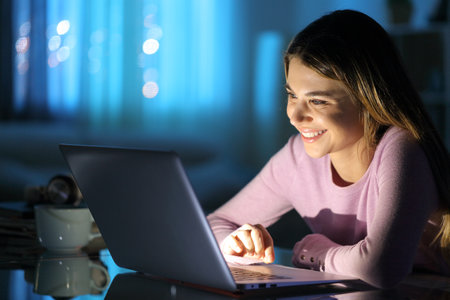 Happy woman watching media on laptop at home in the nightの写真素材