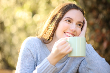 Happy woman drinking coffee in a park looking away at sunriseの写真素材