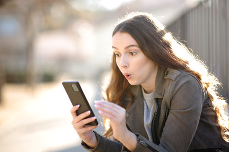 Surprised woman looking at her phone in the streetの写真素材