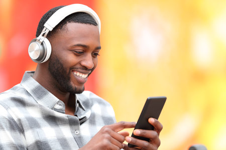 Happy black man wearing headphones listening to music on smartphoneの写真素材