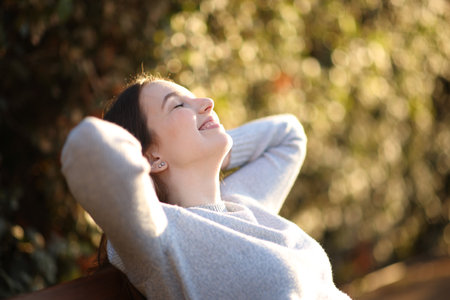 Happy woman resting sitting on a bench smiling in a park at sunsetの写真素材