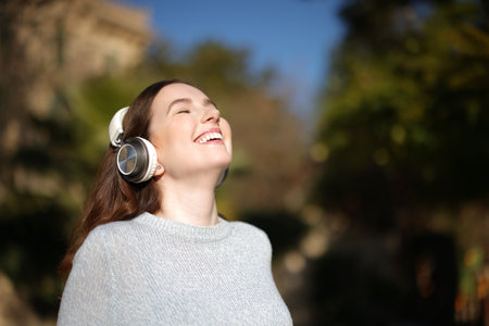 Happy woman breathing fresh air and laughing listening audio with headphones in a parkの写真素材