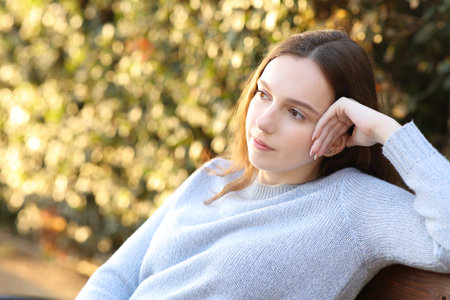 Pensive woman contemplating sitting on a bench at sunset in a parkの写真素材