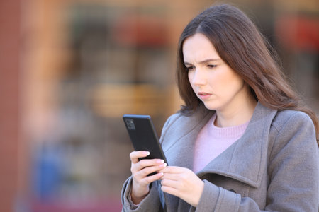 Worried woman using phone walking on the street in winterの写真素材