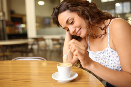Candid woman stirring coffee sitting in a restaurantの写真素材
