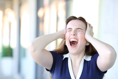 Stressed woman yelling standing in the street with hands on headの写真素材