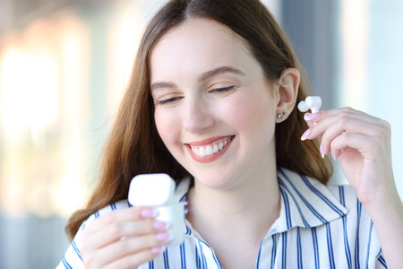 Happy woman putting earbud standing in the streetの写真素材
