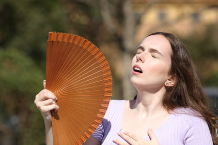 Woman in summer suffering heat stroke and fanning in a parkの写真素材