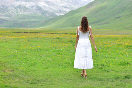 Back view of a woman in white dress walking in natureの写真素材