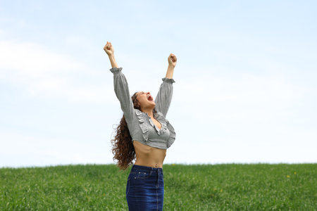Excited woman raising arms celebrating in a fieldの写真素材