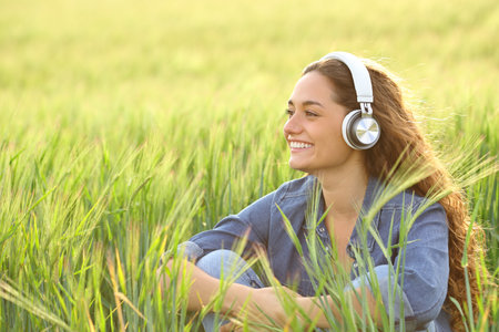 Happy casual woman listening to music wearing headphone in a fieldの写真素材