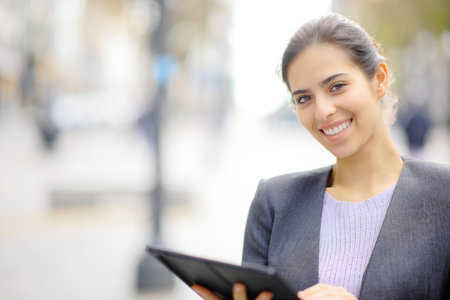 Happy executive posing looking at camera holding tablet outside in the streetの写真素材