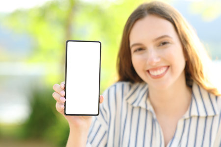 Happy woman showing smart phone screen at camera in natureの写真素材