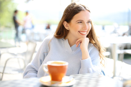Happy woman looks away sitting in a coffee shop terraceの写真素材