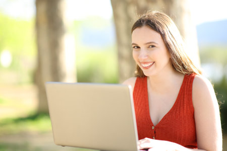 Happy woman looking at you with laptop in natureの写真素材