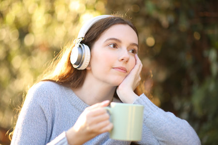 Pensive woman holding coffee and listening to music looking away in a parkの写真素材