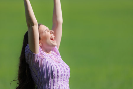Excited woman raising arms and screaming on green in natureの写真素材