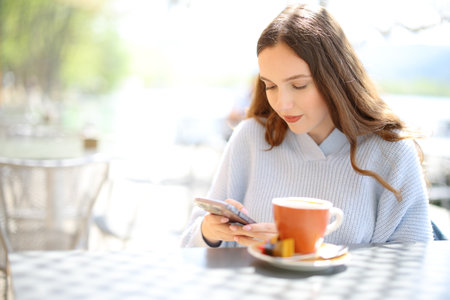 Woman using cell phone sitting in a coffee shop terrace on a sunny dayの写真素材