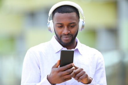 Front view portrait of black man listening to music wearing headphones in the streetの写真素材