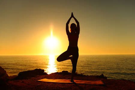 Silhouette of a yogi doing yoga exercise at sunset on the beachの写真素材