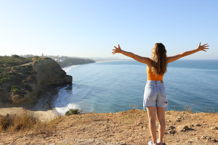 Back view portrait of an excited woman celebrating vacation in a coast outstretching armsの写真素材