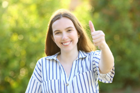 Front view portrait of a happy woman gesturing thumbs up on green in a parkの写真素材