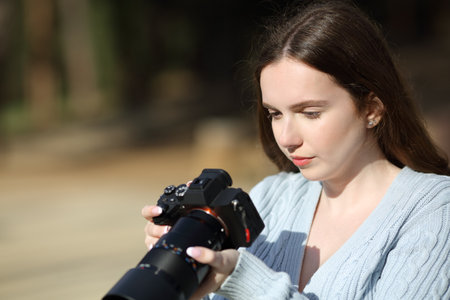 Serious photographer checking pictures on mirrorless camera outdoorsの写真素材