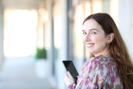 Happy woman twirling looking at camera holding smart phone in the streetの写真素材