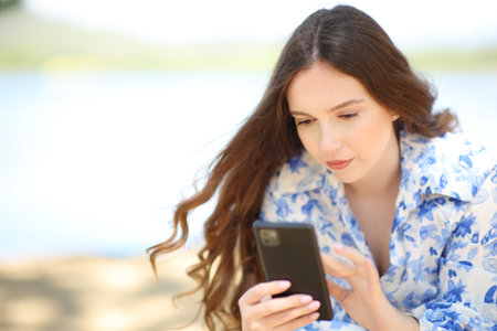 Serious woman sitting on the mountain using phoneの写真素材