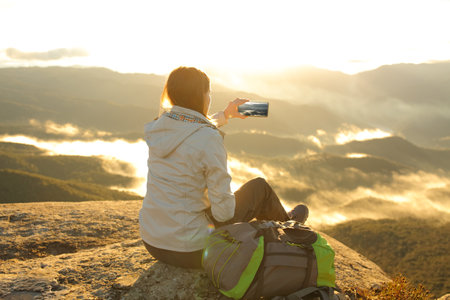Single trekker taking photo of a mountain on smartphone at sunriseの写真素材