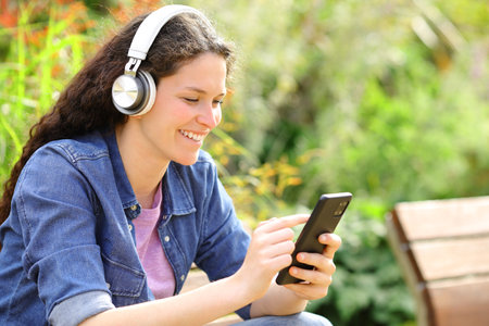 Happy female listening audio content sitting on a bench in a parkの写真素材