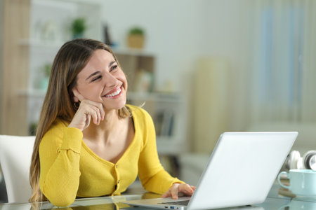 Happy woman at home dreaming looking above with a laptopの写真素材