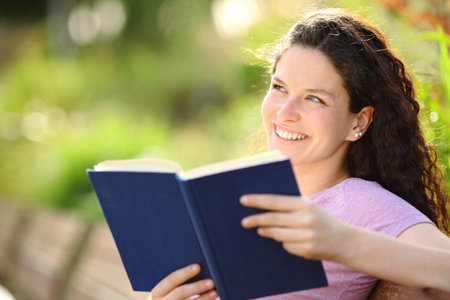 Happy book reader dreaming sititng on a bench in a parkの写真素材
