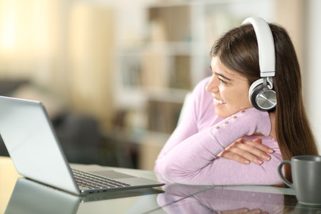 Happy teen watching videos on laptop and headphone sitting at homeの写真素材