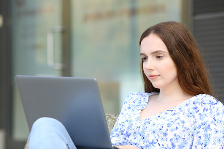 Serious woman sitting in the street using laptopの写真素材