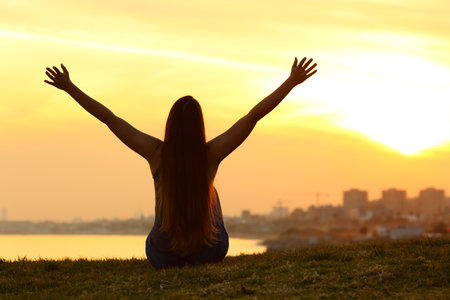 Back view portrait of a silhouette of a woman celebrating at sunset in outskirtsの写真素材