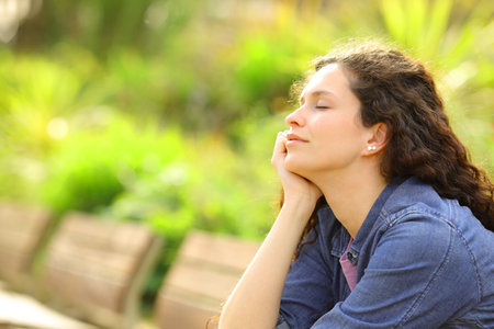Woman relaxing mind closing eyes sitting on a bench in a parkの写真素材
