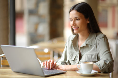 Happy woman using laptop sitting in a terrace of a coffee shop aloneの写真素材