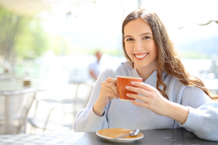 Happy restaurant customer holding coffee cup looking at camera in a terraceの写真素材